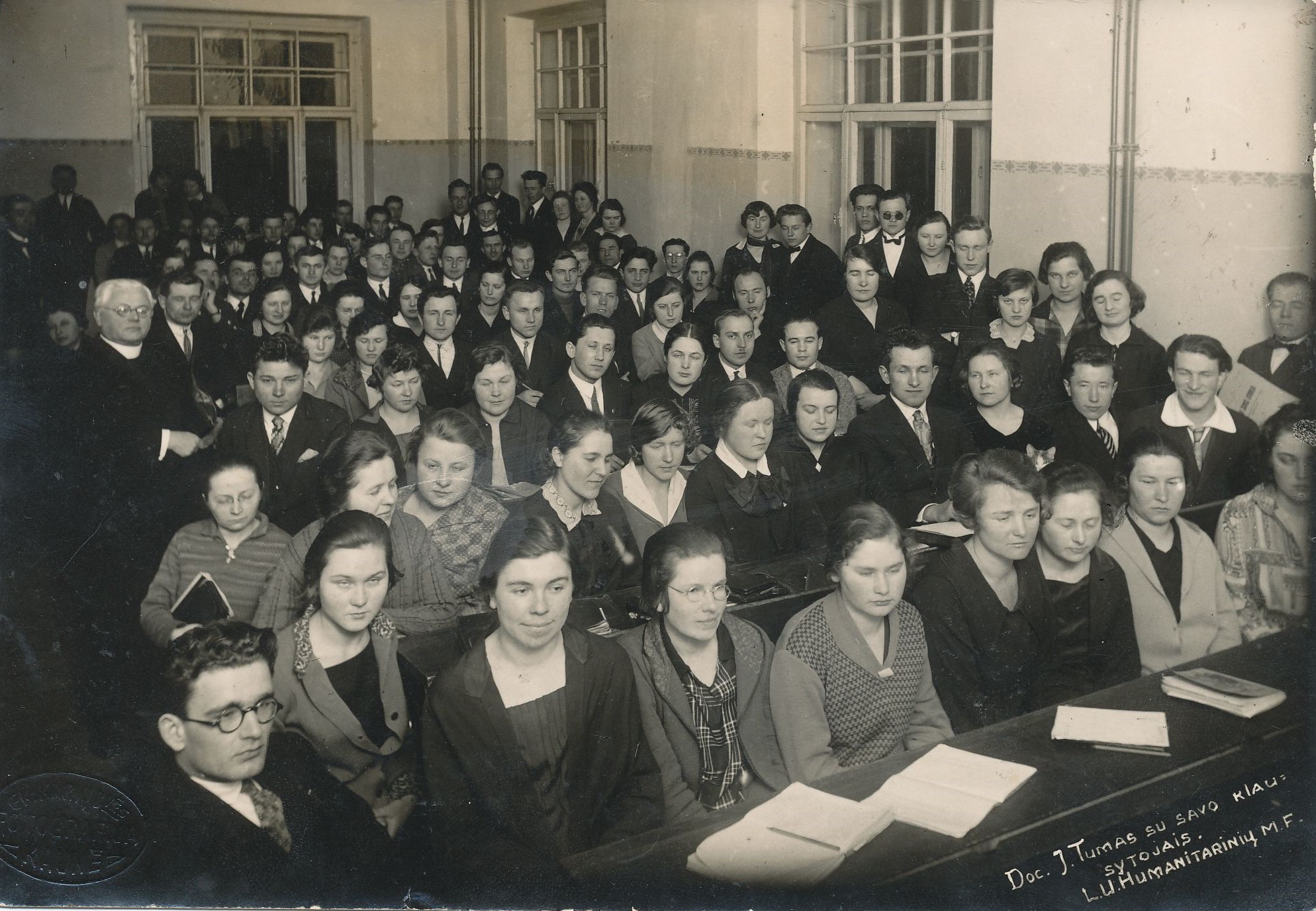 J. Tumas-Vaižgantas su studentais auditorijoje. I-oje eilėje pirmas iš kairės sėdi P. Papečkys; II-oje eilėje pirma iš kairės Veimerytė; III-oje eilėje ketvirtas iš kairės L. Skabeika; IV-oje eilėje pirmas iš kairės Vaižgantas. Kaunas, 1927 m. MLLM 27000