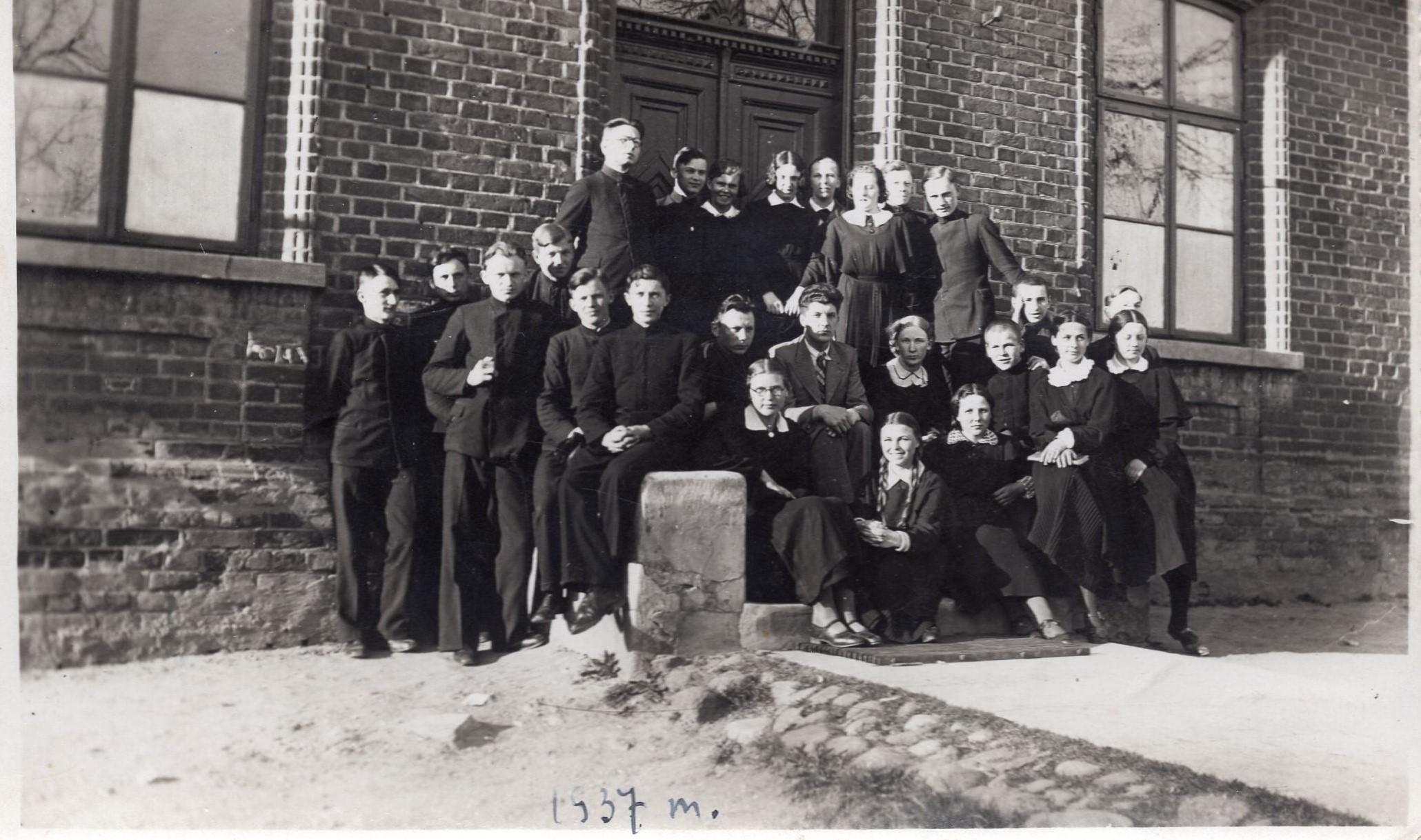 Lietuvių kalbos mokytojas B. Palekas (centre), šalia jo – K. Bradūnas, J. Švabaitė sėdi ant laiptelio trečia iš dešinės. Vilkaviškis, 1937 m.  MLLM 109179