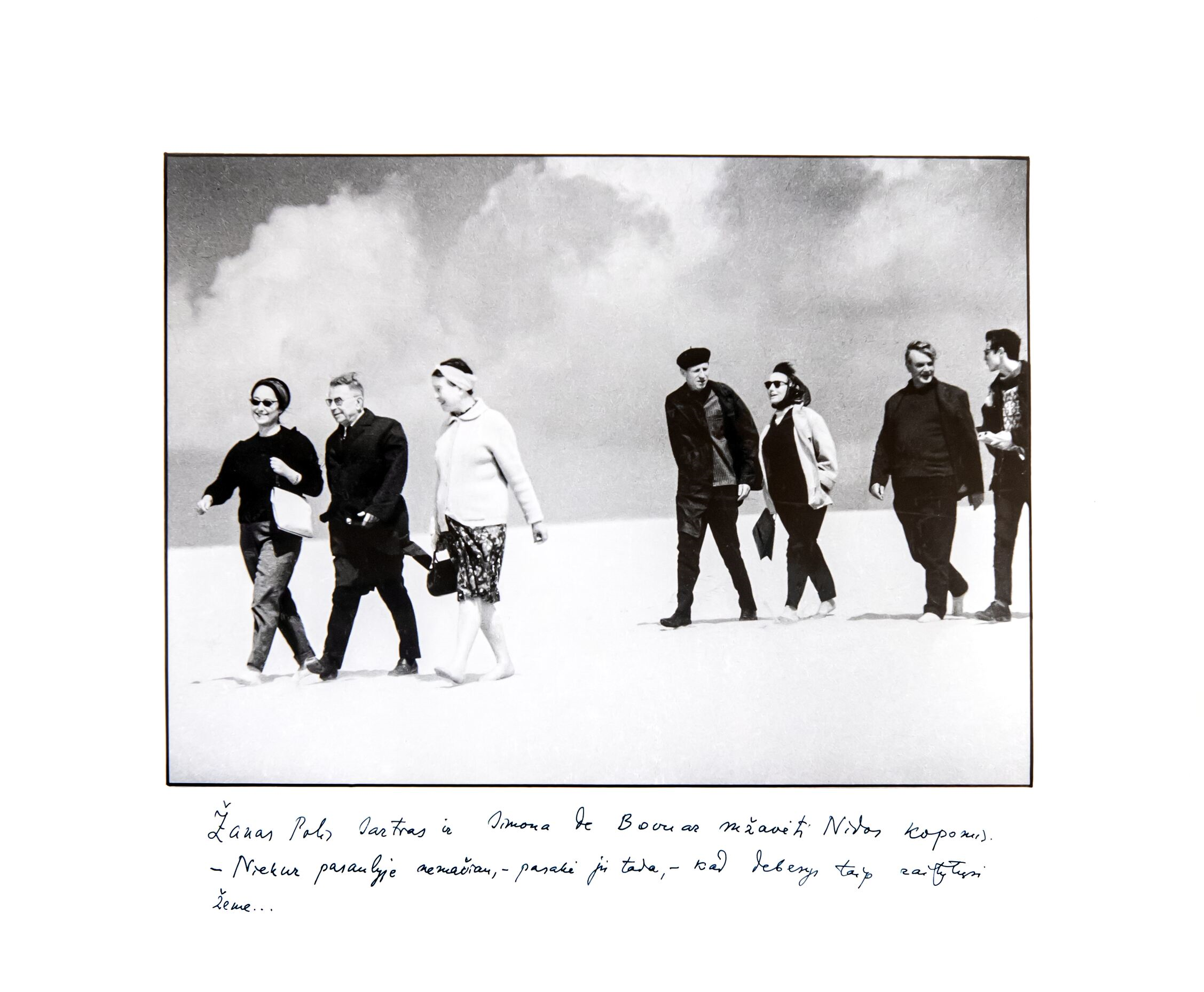 Iš kairės:  L. Zonina, Ž. P. Sartras, S. de Bovuar, M. Sluckis, E. Mieželaičio žmona S. Mieželaitienė, E. Mieželaitis ir neišaiškintas vyras. Nida, 1965. Po nuotrauka – E. Mieželaičio užrašas. RMM ĮK 12476/5