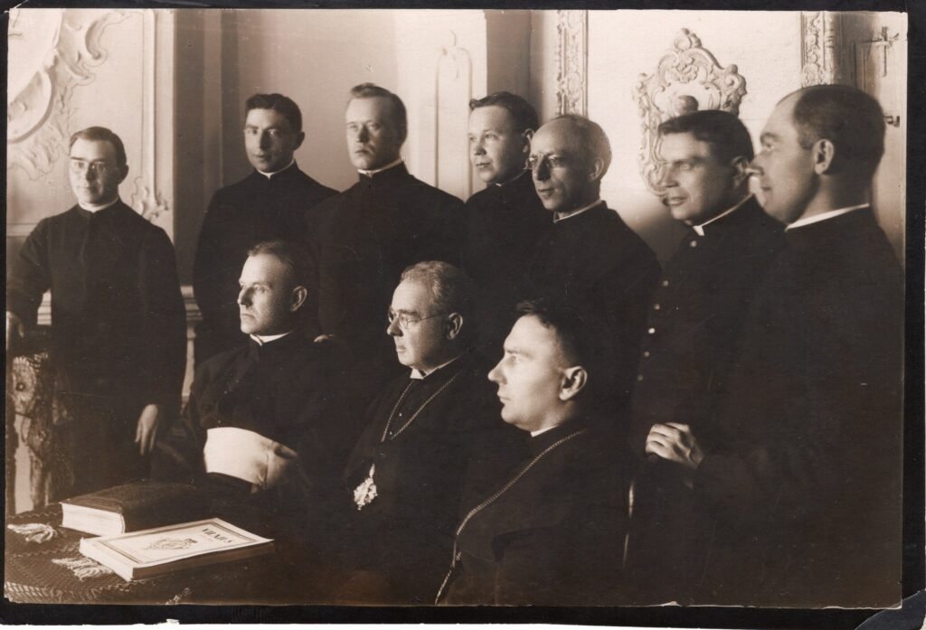 Foto kopija. Kauno Kunigų seminarijos profesoriai Maironio namuose, apie 1924 m. Sėdi iš kairės: K. Paltarokas, Maironis, B. Čėsnys. Stovi iš kairės: B. Andruška, S. Gruodis, M. Morkelis, Dr. S. Ūsoris, Z. Meškauskas, T. Brazys, Z. Petrošius. MLLM 130534