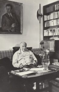 J. Grušas savo darbo kabinete. Kaunas, 1976 m. R. Rakausko nuotrauka. Kambario kampe atremta alebarda.